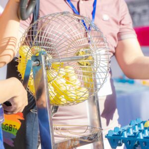 Two people engaging in a bingo game, spinning a cage in a lively, outdoor setting.